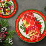 Red poinsettia patterned disposable dinner plates, dessert plates, and folded napkins for a Christmas party setting.