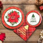 Red poinsettia patterned disposable dinner plates, dessert plates, and folded napkins for a Christmas party setting.